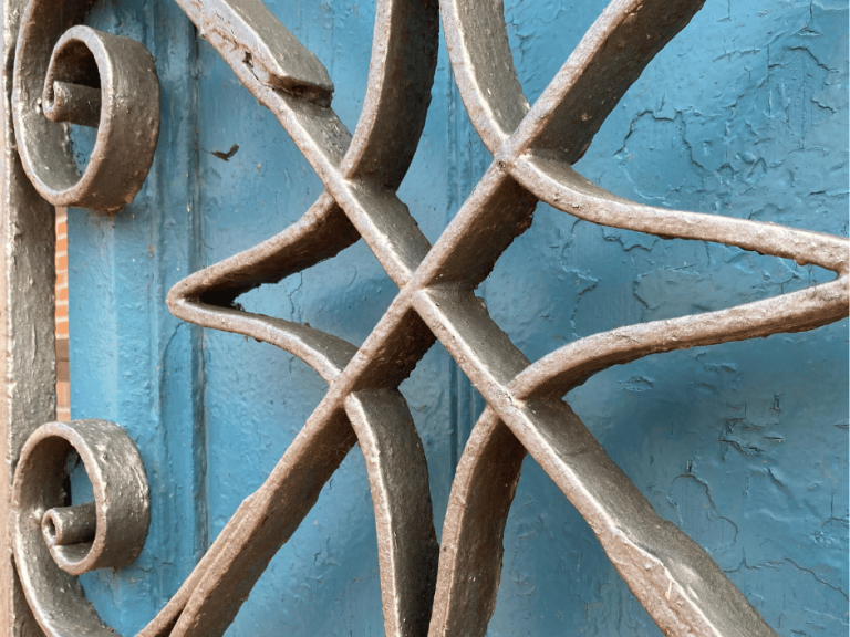 Ein schmiedeeisernes Ornament vor einer etwas verwitterten blauen Holztür