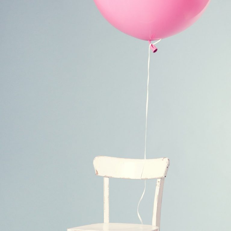 Ein weißer Holzstuhl an dem ein Rosafarbener schwebender Ballon gehängt ist